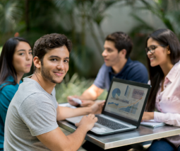 Grupo de estudiantes sentados en mesa en un patio mirando una computadora