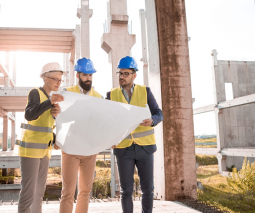 3 ingenieros parados frente a una construcción mirando un plano