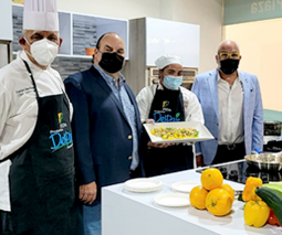 4 personas paradas frente a una cocina mostrando un plato recién confeccionado