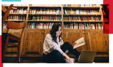 persona sentada en el piso leyendo frente a un anaquel de libros