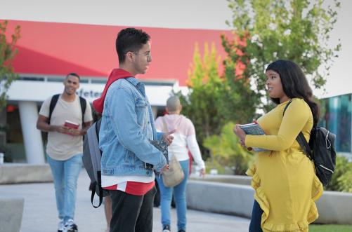 dos estudiantes parados conversadose frente a una de las facilidades de la universidad